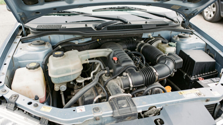 Compartiment moteur d’une voiture d’occasion ouvert, avec le vase d’expansion, les durites du radiateur et une légère fuite de liquide de refroidissement visibles.